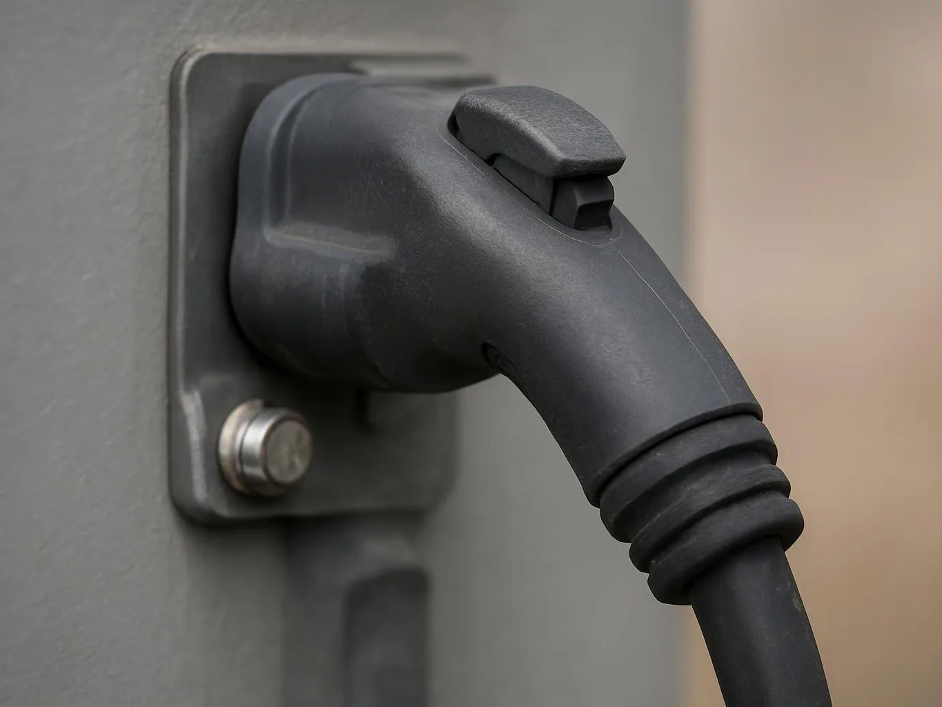 A black charging plug is inserted into a gray wall-mounted socket with a metal screw visible