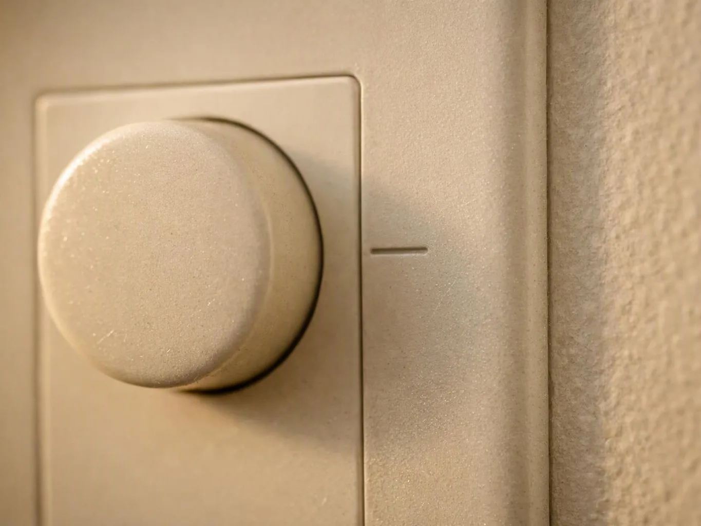 Close-up of a beige wall dimmer switch with a round knob beside textured wall paint