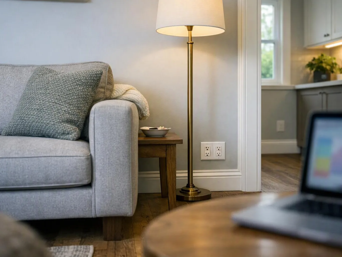 A gray sofa sits beside a lit floor lamp and a small wooden table in a cozy living room