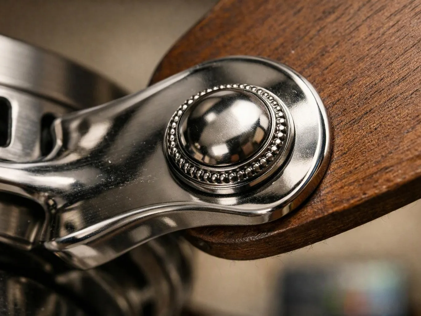 A shiny metal hinge with a round ball joint connects to a wooden chair arm close up