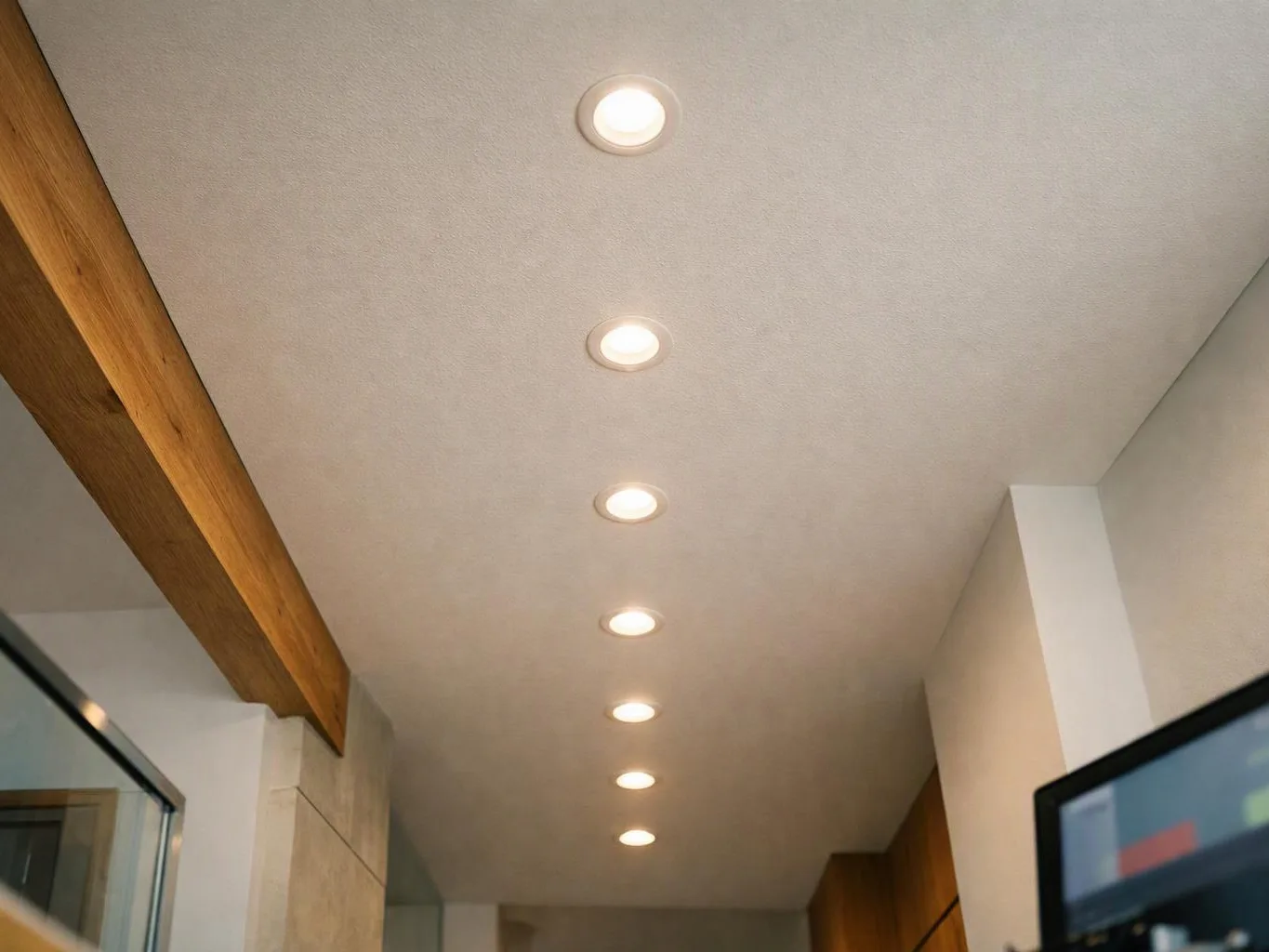 A white ceiling with a row of recessed lights stretches through a modern interior hallway