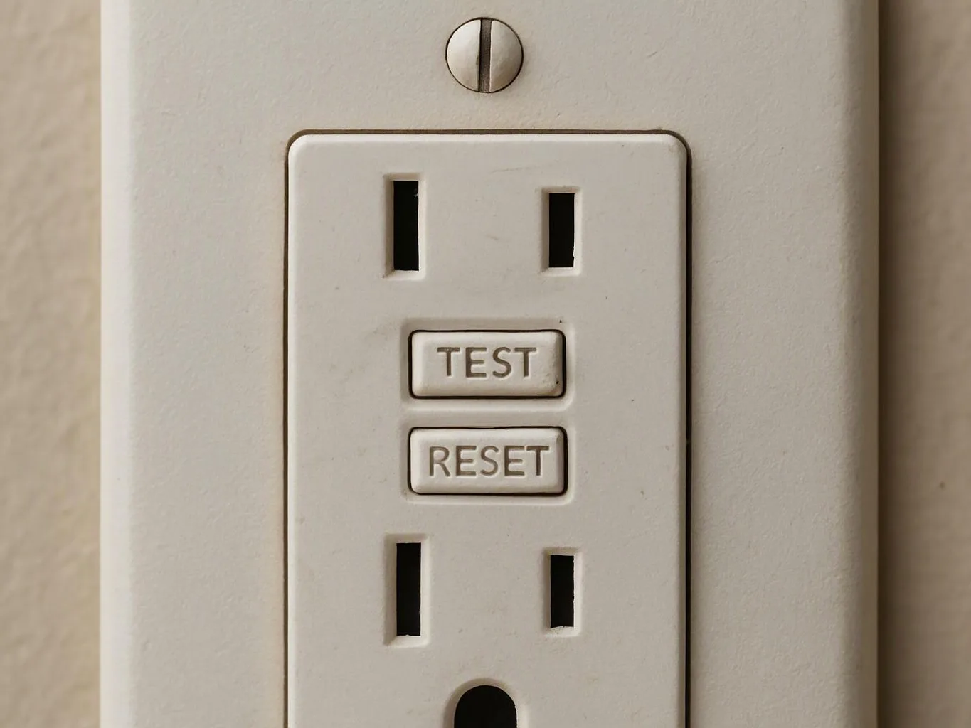 A white GFCI electrical outlet with TEST and RESET buttons is mounted on a beige wall